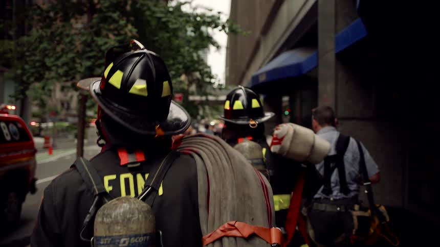 A group of firefighters in full gear and helmets walk on a city street