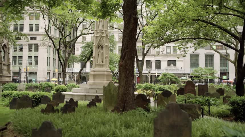 Tombstones in a public square with the monument in the center and urban buildings in the background