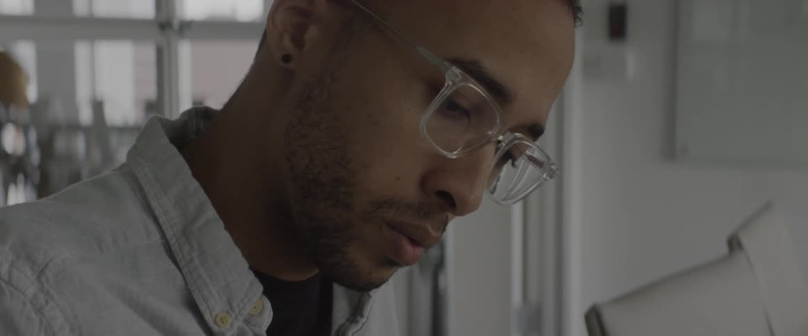 Man wearing glasses is sitting at desk and staring downwards