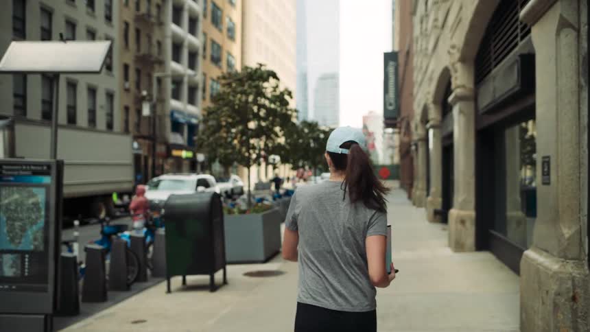 A woman walks along a sidewalk in a metropolitan city during daytime