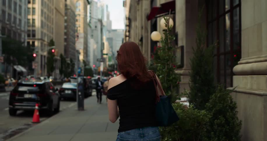 Redhaired woman with a bag walking on the sidewalk of an urban street in a metropolis