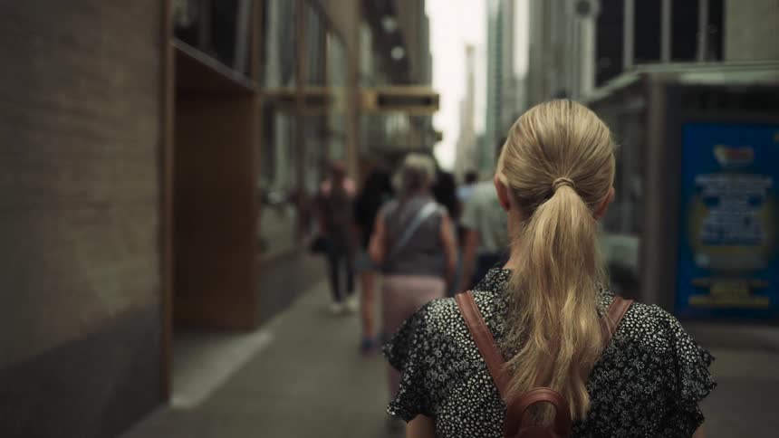 Blonde woman walking through the streets of a metropolis with other pedestrians