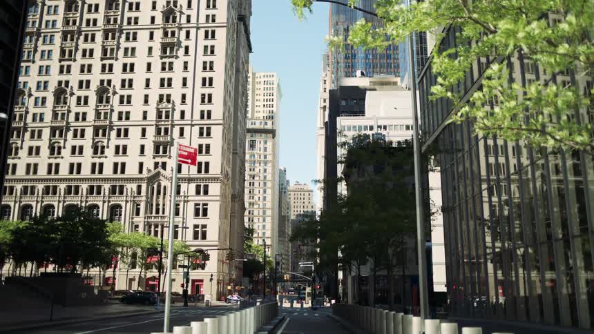 A quiet city street is lined with tall buildings and green trees under clear daylight