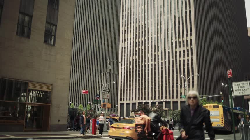 In a bustling timelapse pedestrians hurry across the street as taxis a city bus and other traffic speed through a new york city intersection