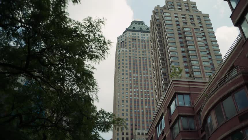 A lowangle driving shot looks up at skyscrapers including the allianz building framed by older brick buildings and trees