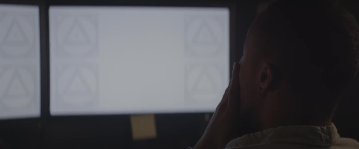 A man sits at a desk with two monitors on