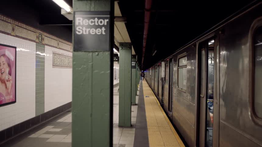 A smooth tracking shot moves along the platform of the rector street subway station passing green pillars next to a stationary train