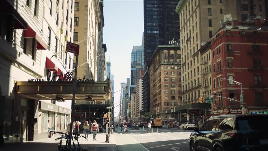 People walk and cycle down a busy city street lined with tall buildings