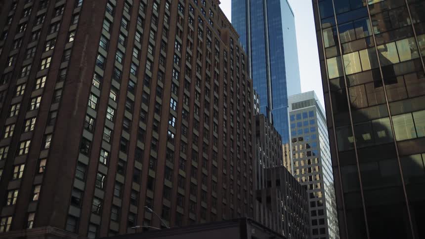 A lowangle view from a moving vehicle captures a mix of modern glass skyscrapers and older brick buildings in a dense city