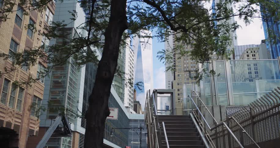 A moving shot passes a city tree revealing stairs and the one world trade center standing tall amongst modern and classic architecture