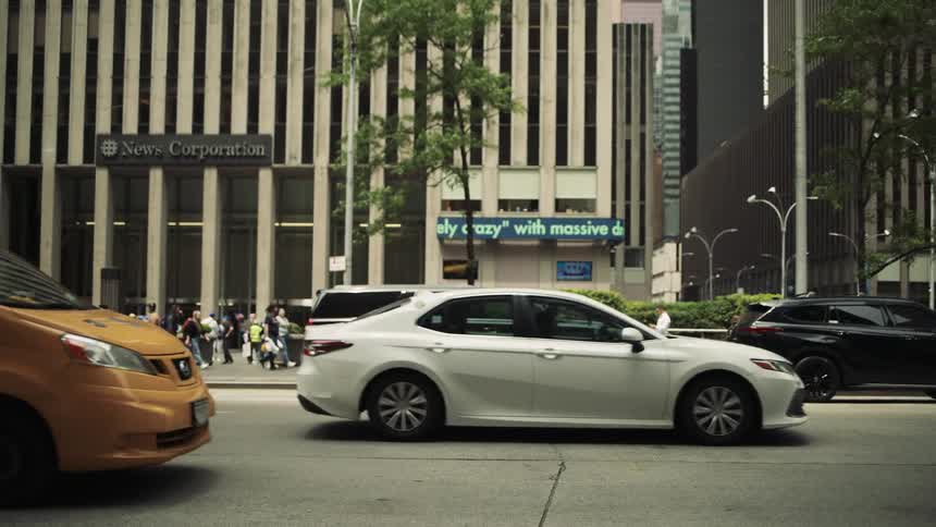 Vehicles drive on the road as people walk past