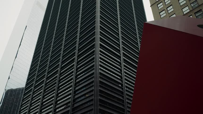 A modern building with a dark facade and numerous vertical white lines rises against a light sky flanked by other tall buildings on either side