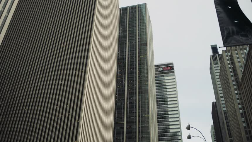 Tall office buildings rise against a gray sky in a dense cityscape