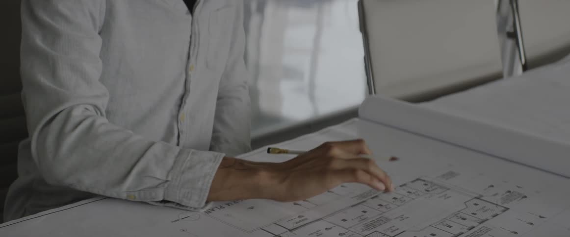 A person sitting at a desk looking and writing on some blueprints