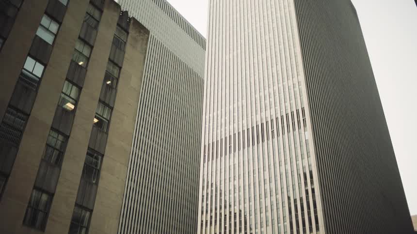 A groundlevel view of a vibrant city street dominated by a cluster of imposing skyscrapers that rise towards the sky on the left a more traditional building with numerous windows contrasts with the modern sleek facades of the taller structures