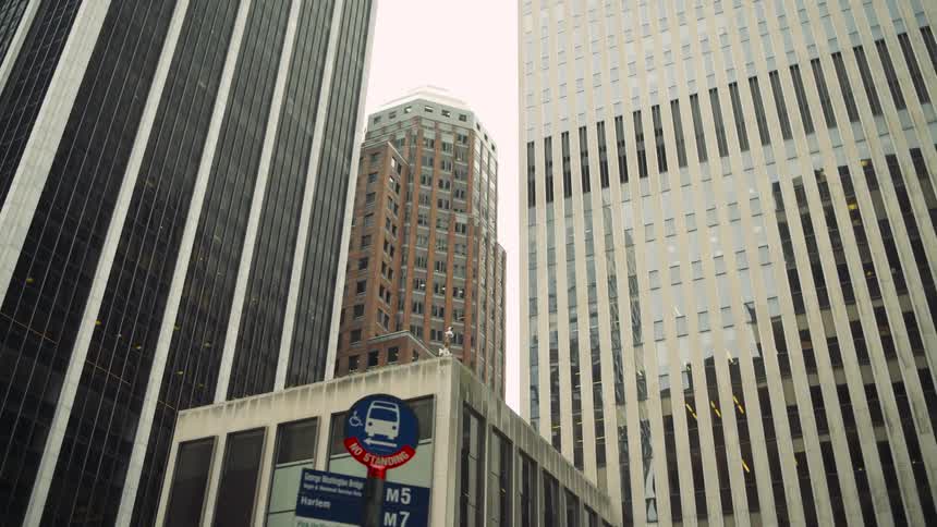 Tall skyscrapers tower above a bus stop sign in a bustling city