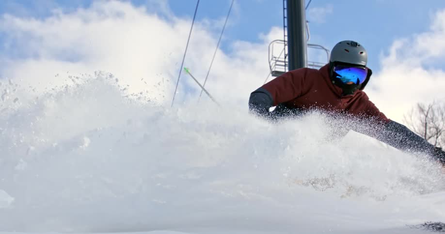 A person skiing downhill turns sharply which causes snow to be kicked up