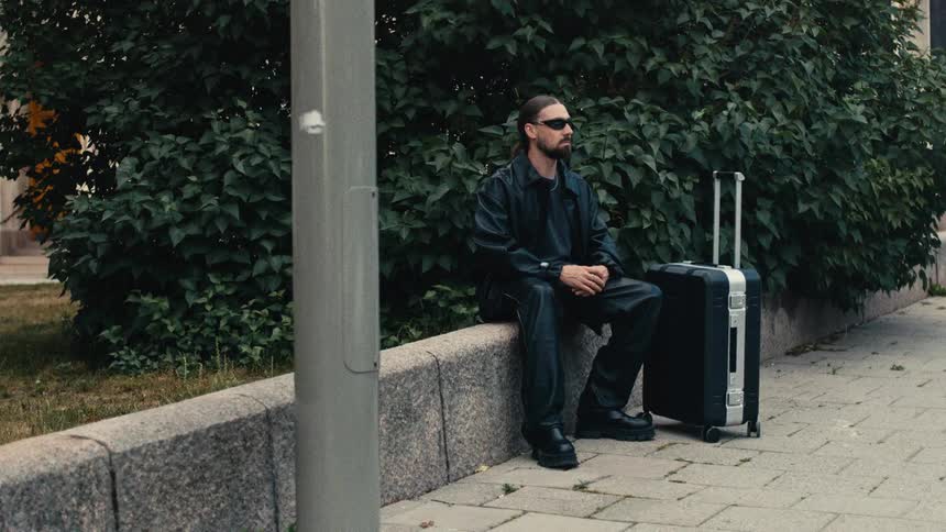 A man sits on a sidewalk with a suitcase beside him