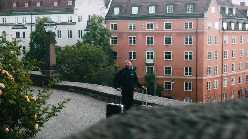Man standing on sidewalk pulling two large suitcases in front of old residential buildings