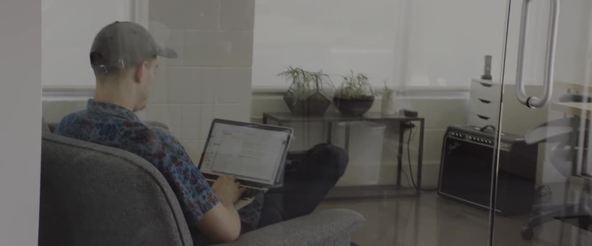 A man sits in an armchair and works on a laptop