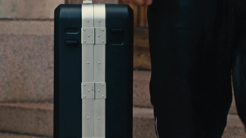 A person walks down a staircase leaving a suitcase behind