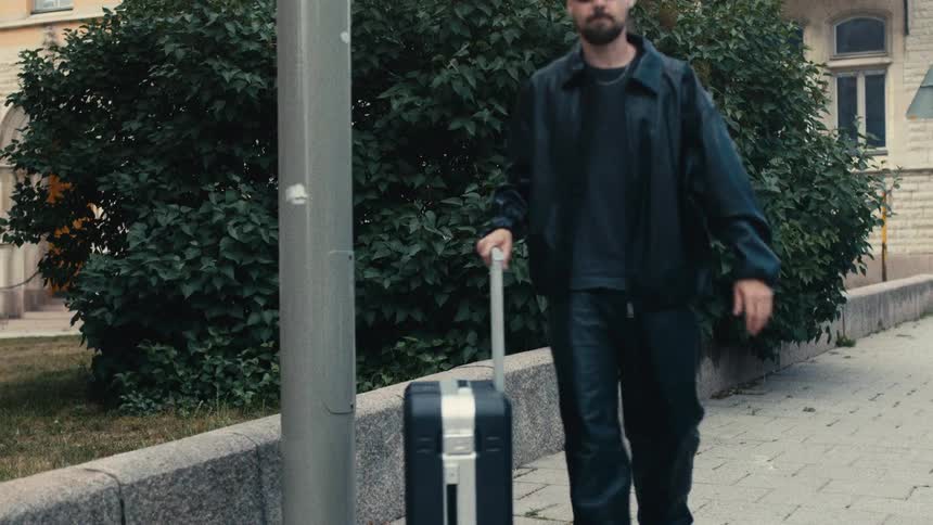 A man walks on the sidewalk pulling a suitcase