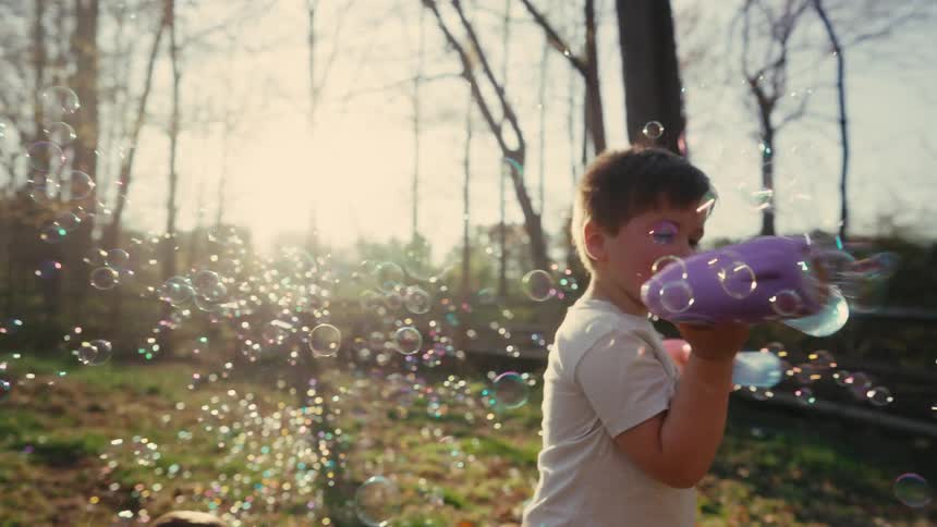A baby is playing with a bubble shooter and the sun behind him makes the scene beautiful