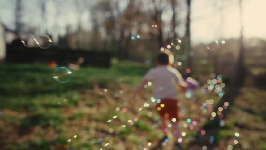 Happy little boy laughing and running spraying bubbles in the backyard