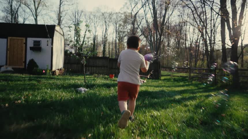 Child plays with soap bubbles while a baby watches from a striped blanket in the backyard