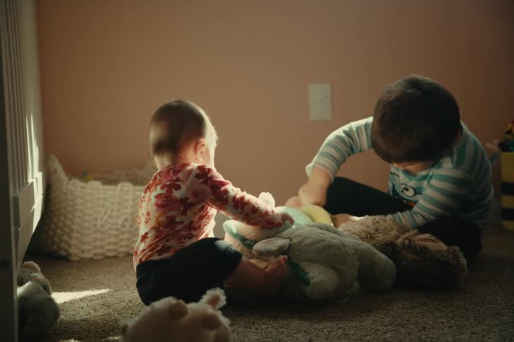 Two young children play with stuffed animals on a carpeted floor