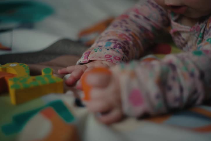 Baby in flowery clothing plays with colorful pieces on a soft surface