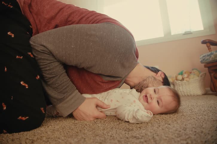 A man plays affectionately on the carpet with a smiling baby
