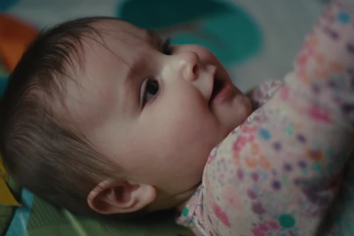 Baby lying down with curious expression and big eyes wearing colorful flowery outfit
