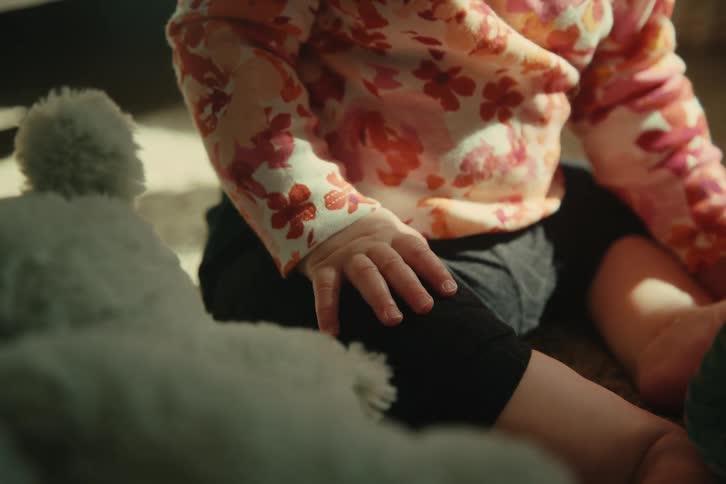 Baby sitting on the carpet waves its hand