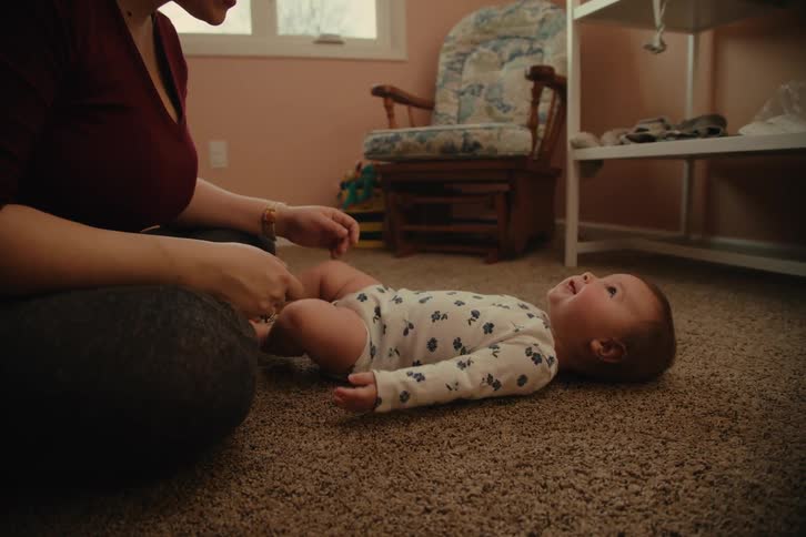 Woman gently playing with baby lying on carpeted floor in a nursery