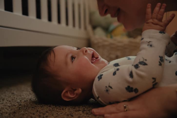 Mother lovingly kissing her baby girl who is lying on the carpet in a room