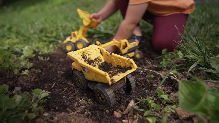 Close up of a female child playing with toy vehicles while sitting on a lawn outdoors during daytime