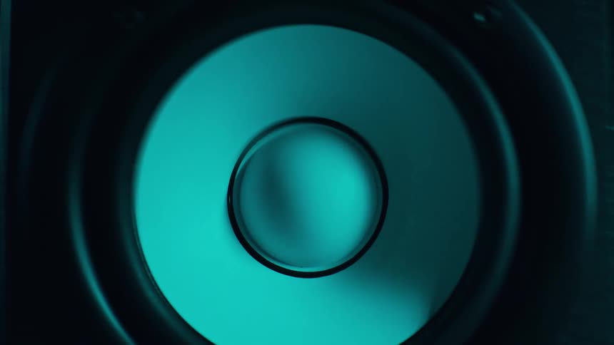 Close up of a speaker woofer as it plays music in a blue lit room