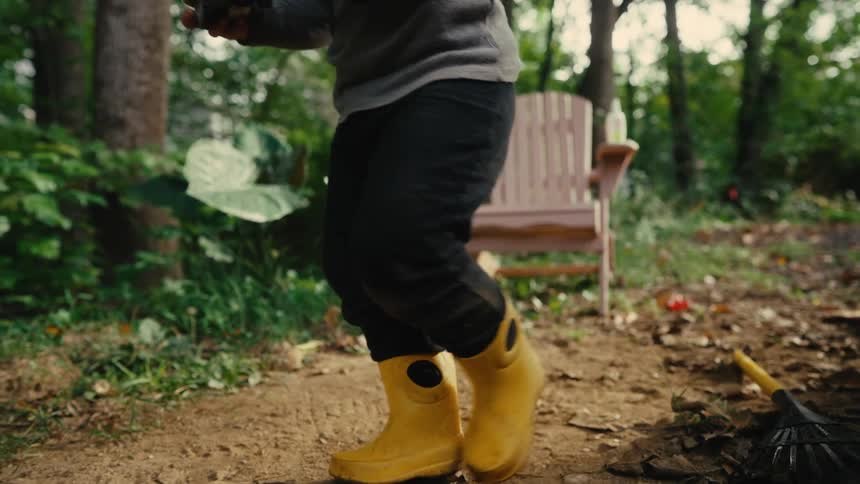 The boy picks up his toy and walks over to the wheelbarrow