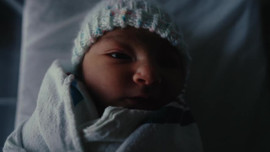 A newborn baby lies swaddled in a blanket wearing a knit hat