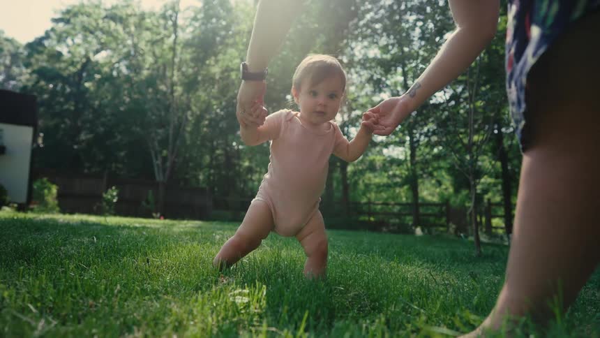 Mother in grassy backyard teaching little daughter to walk