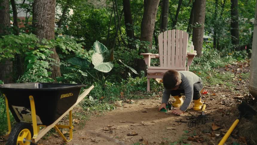 Boy in a wooded yard playing with a toy farm vehicle