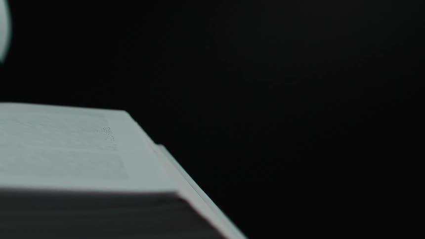 A closeup shows the pages of an open book being flipped against a dark background