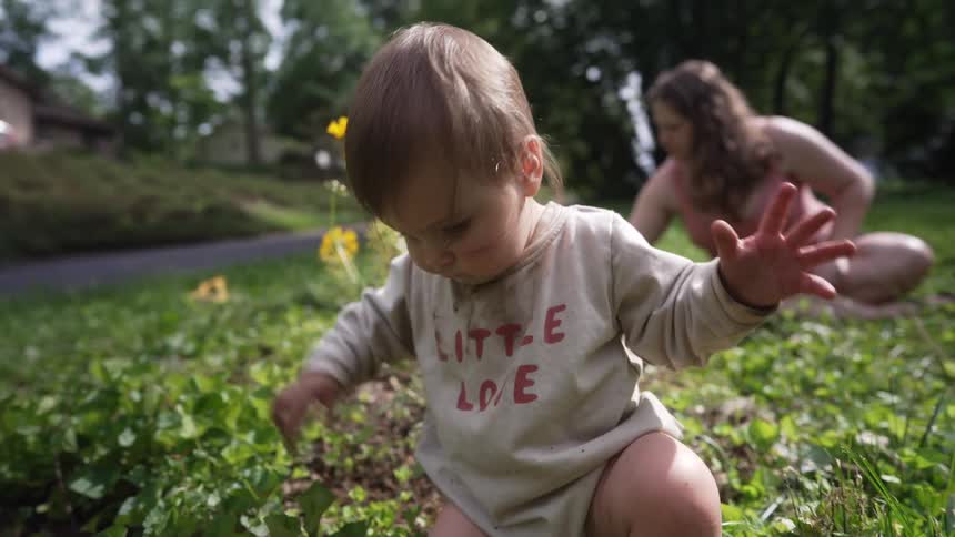 Baby playing in a vegetable garden with mother sitting in the background