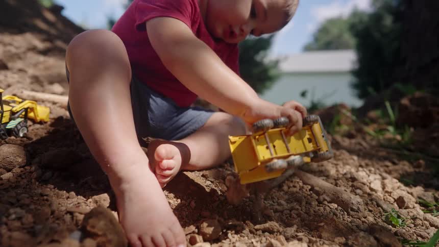 The boy lifts dirt with his toy dumptruck