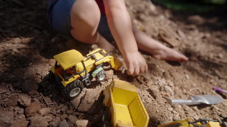 The child lifts dirt and drops it on his toy truck