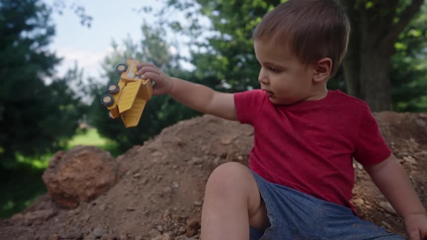 The boy pours soil out of his toy dump truck
