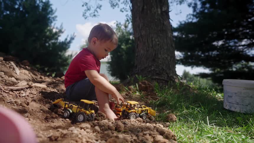 A young boy plays with toy construction trucks in the dirt