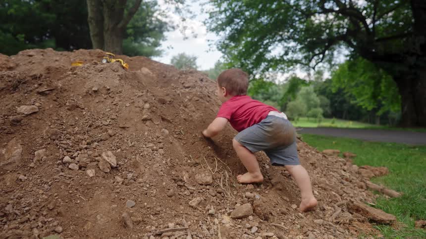 Toddler climbing a large dirt mound in a grassy outdoor setting