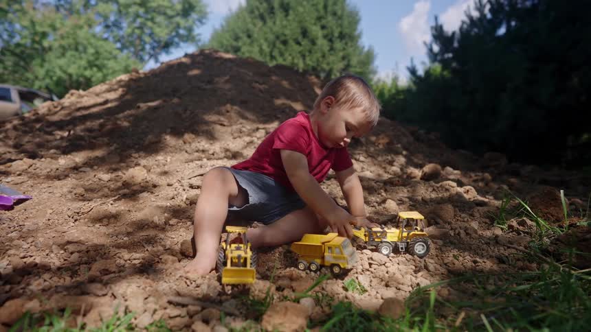 The boy drags the toy truck across the dirt